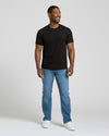 Man wearing a black t-shirt, blue jeans, and white sneakers on a plain background. MODEL_INFO: Model is 5'8" wearing size M short