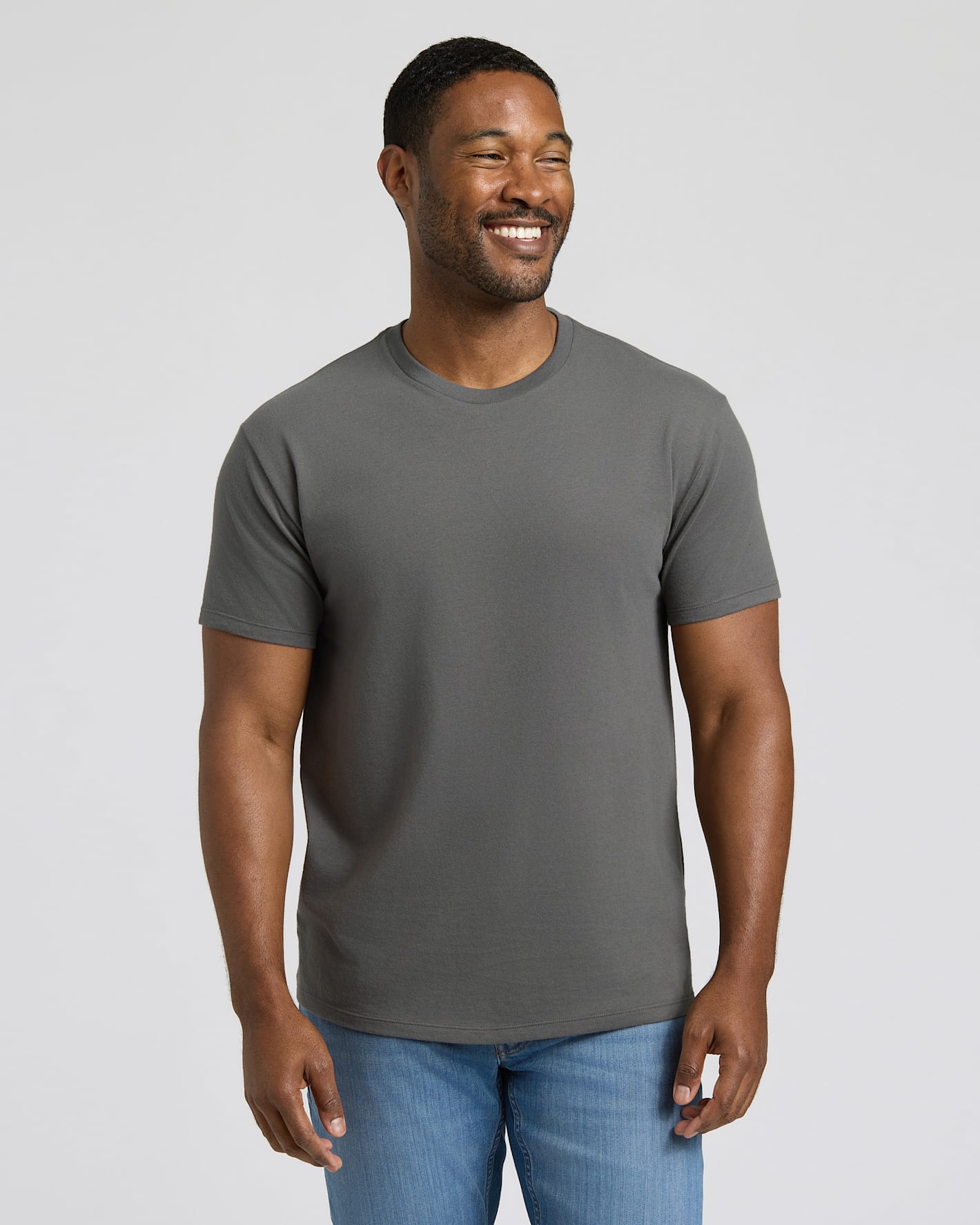 Man wearing a gray t-shirt and blue jeans against a plain background