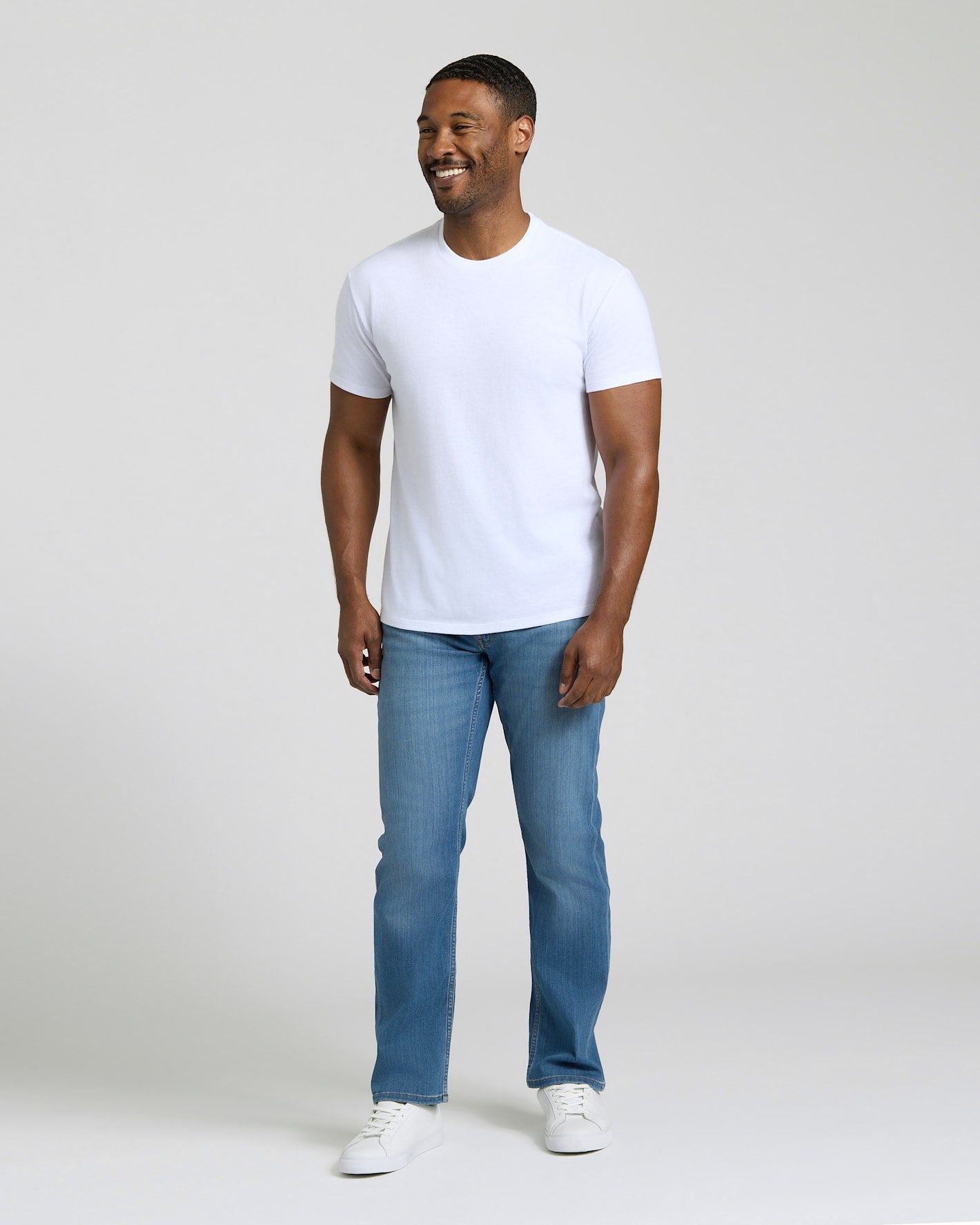 Man wearing a white t-shirt and blue jeans on a plain background. MODEL_INFO: Model is 5'8" wearing size M short