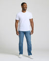Man wearing a white t-shirt and blue jeans against a plain background. MODEL_INFO: Model is 5'8" wearing size M short