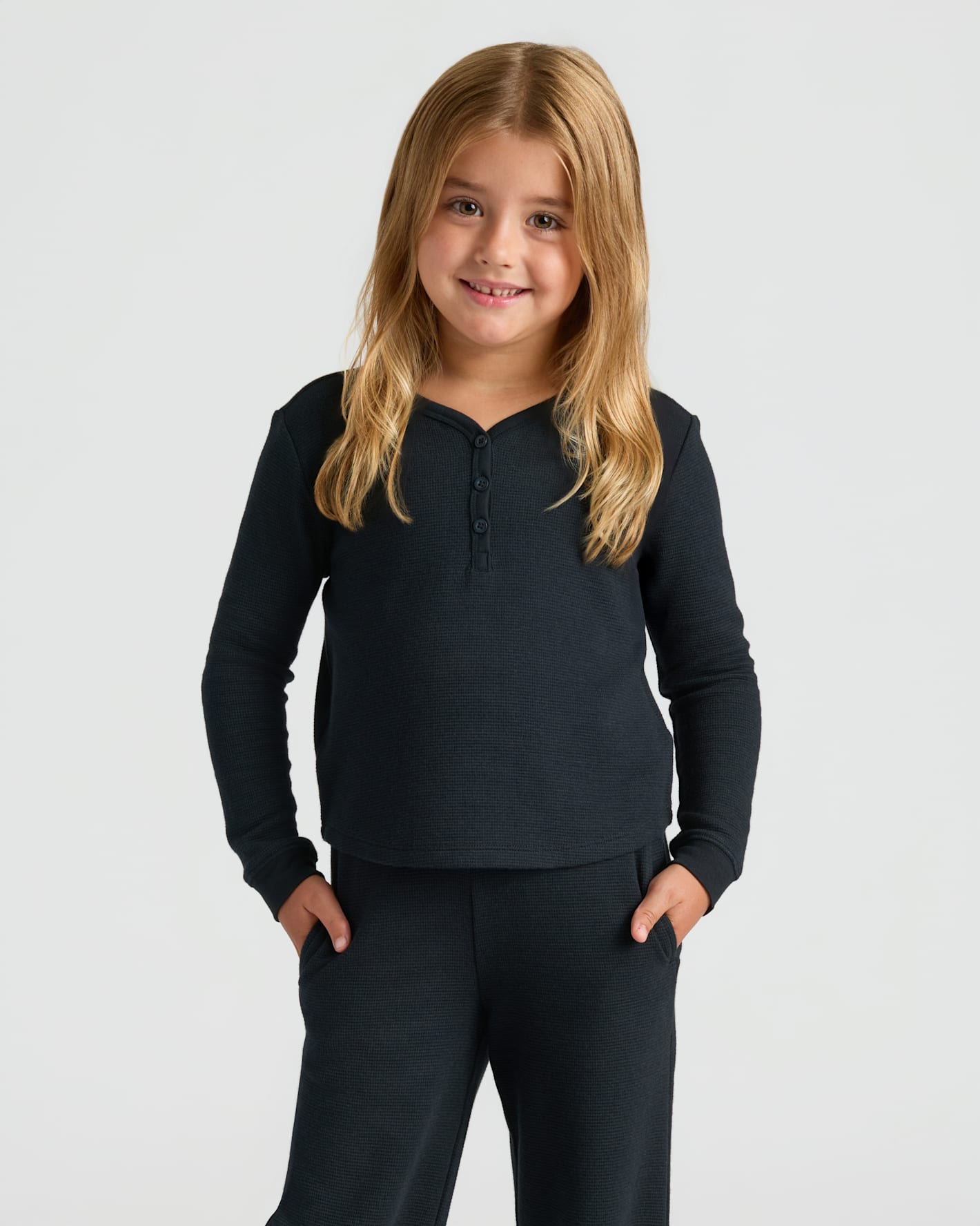 Girl in Girls Long Sleeve Boxy Waffle Henley, black, smiling, hands in pockets.