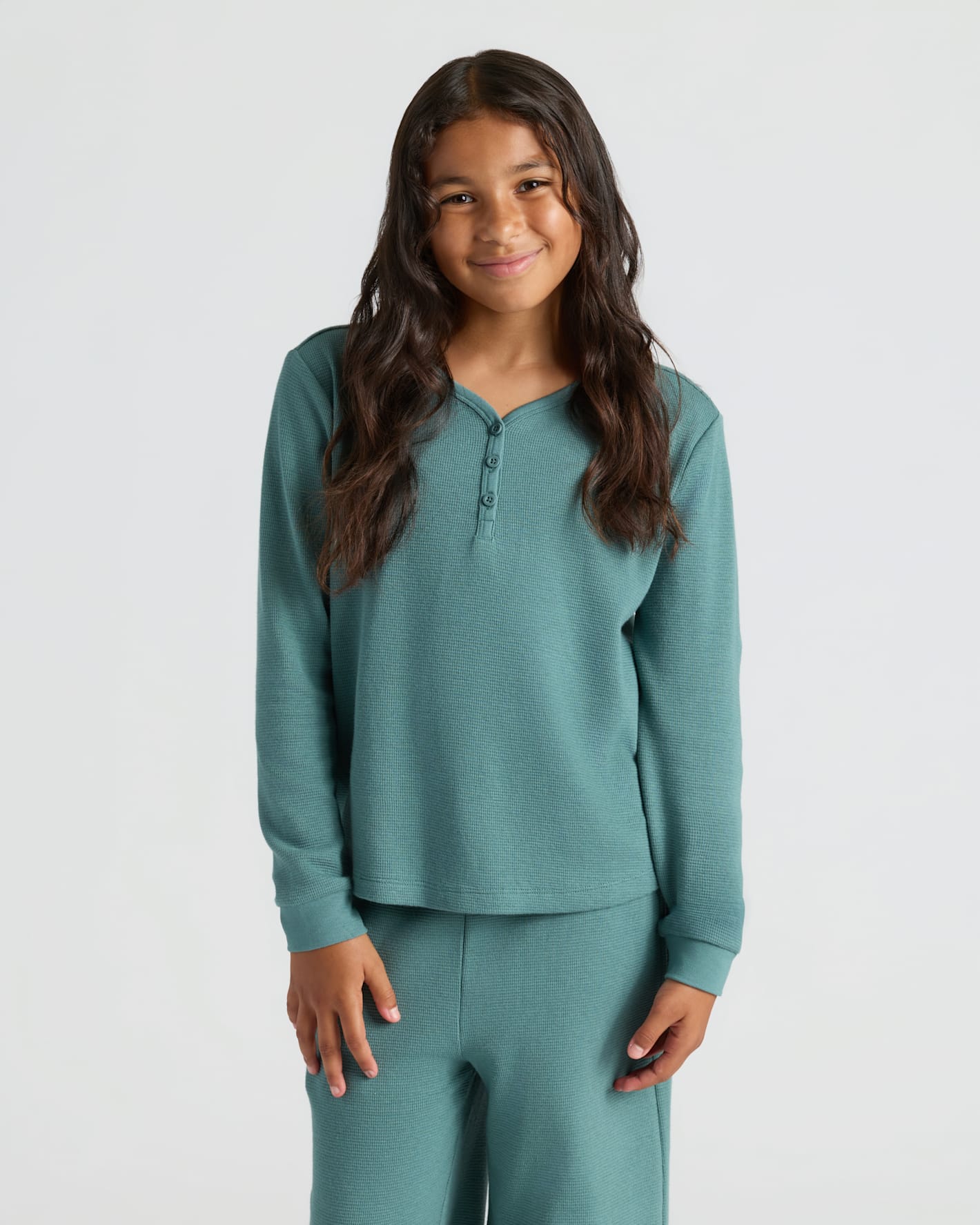 Girl in teal Girls Long Sleeve Boxy Waffle Henley, smiling gently.