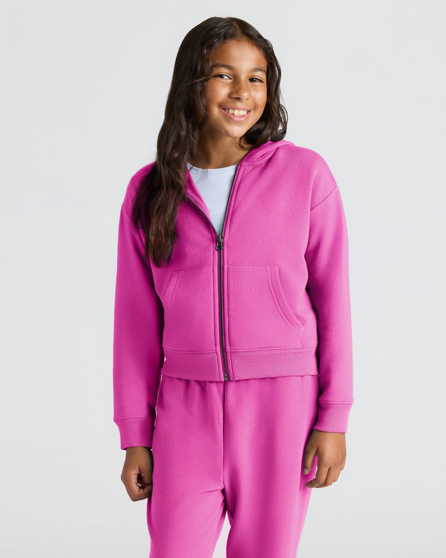 Girl in Girls Electric Fuchsia Cropped Zip Hoodie & Relaxed Joggers, smiling.
