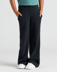 True ClassicChild wearing Girls Black Waffle Long Sleeve Henley & Pants, hands in pockets.