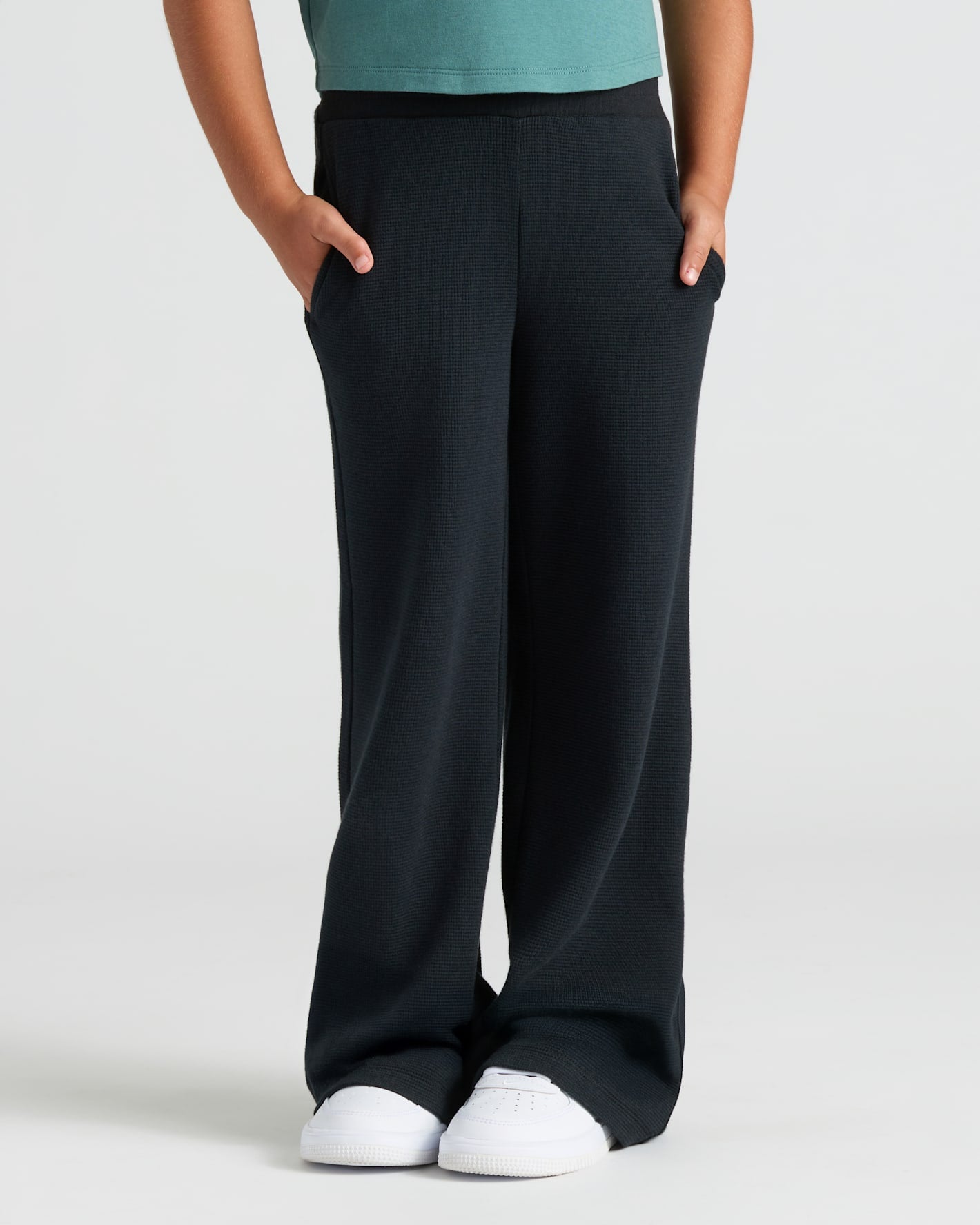 Child wearing Girls Black Waffle Long Sleeve Henley & Pants, hands in pockets.