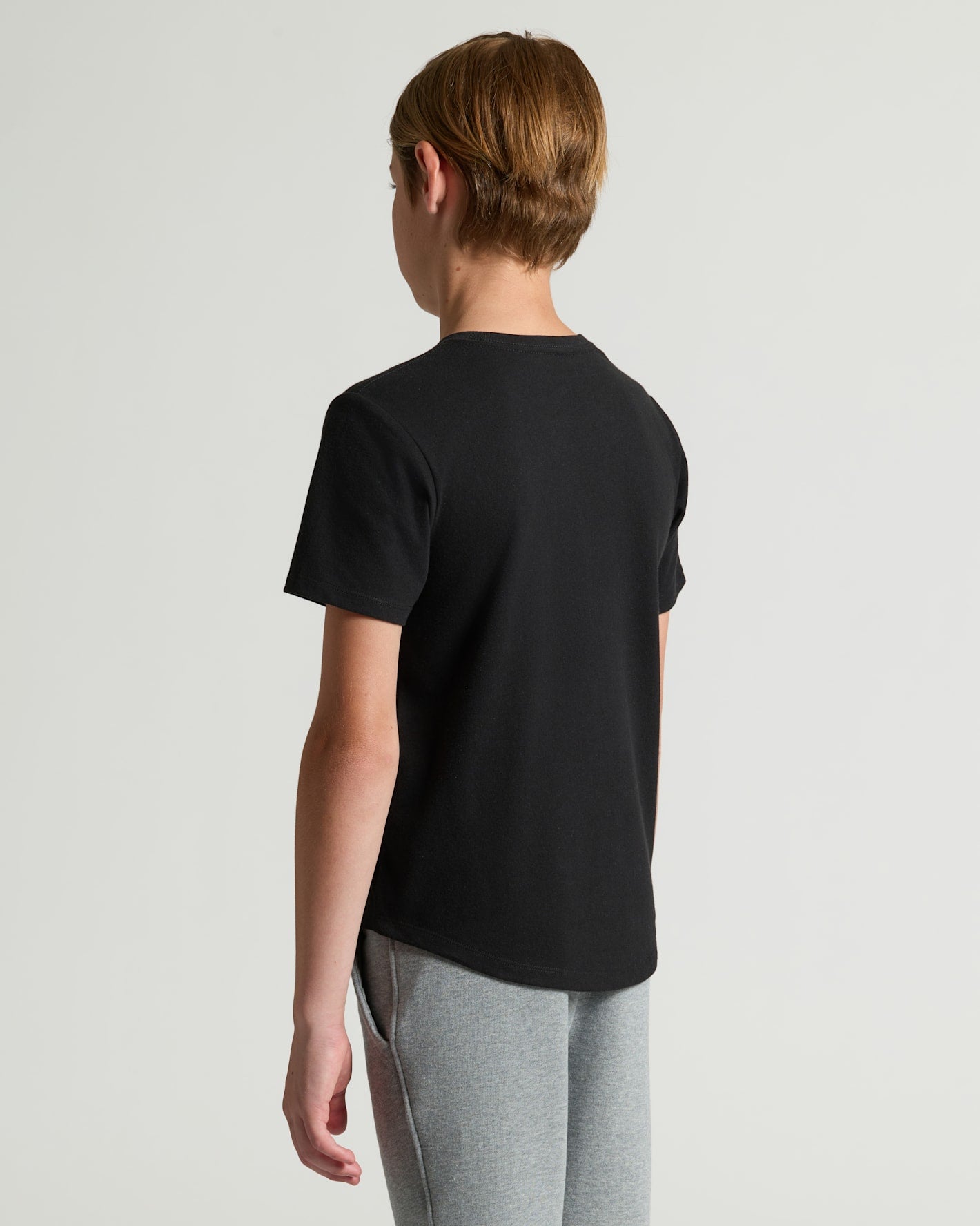 Teen wearing Boys' Classic Curved Hem Crew Neck 3-Pack, black tee, gray pants.