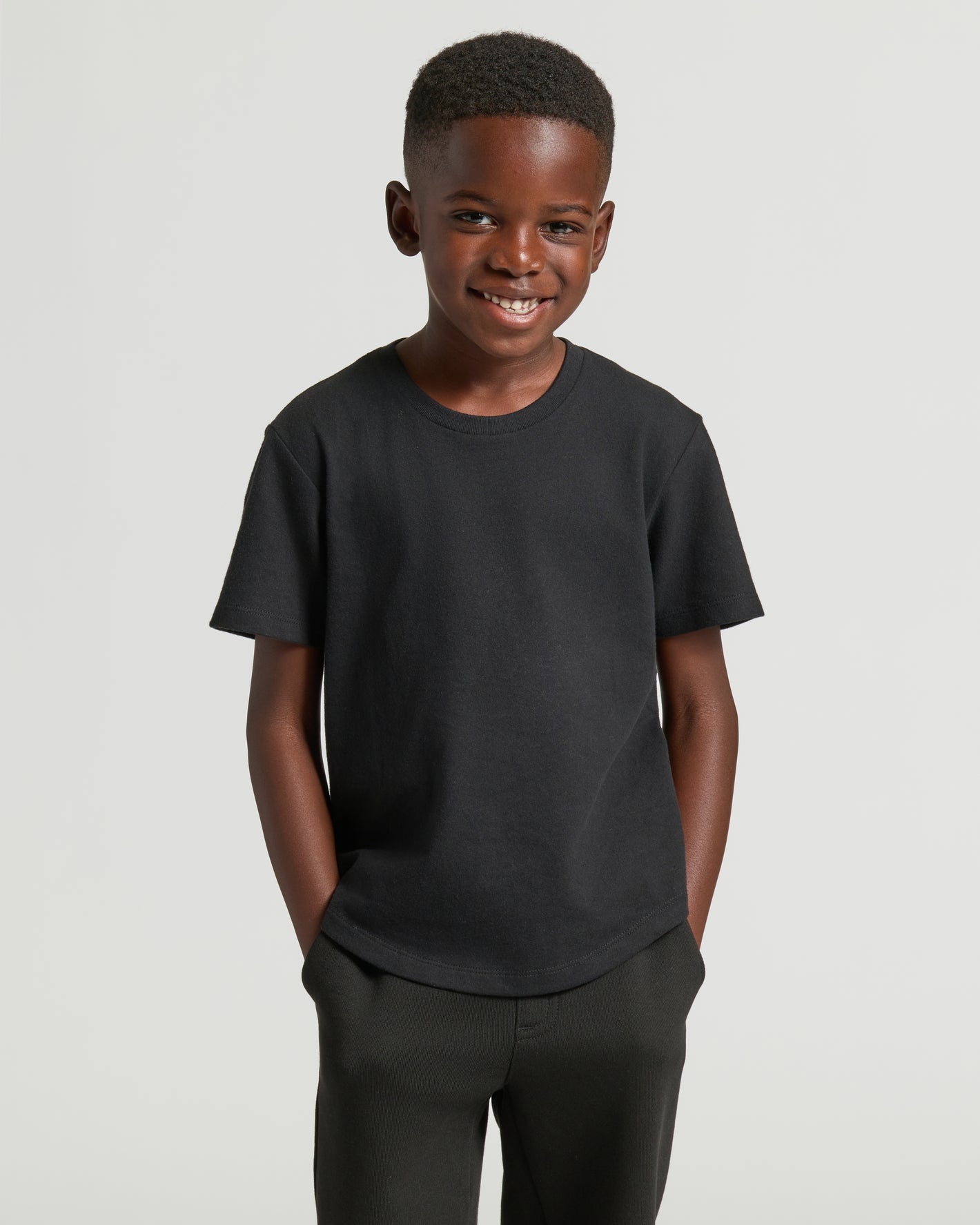 Boy wearing Boys' Black Classic Curved Hem Crew Neck with hands in pockets.