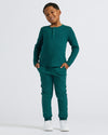 Boy in Boys Deep Emerald Long Sleeve Waffle Henley, smiling, hands in pockets.
