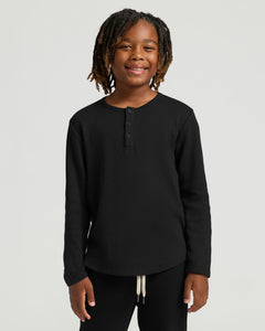 True ClassicChild wearing Boys' All Black Waffle Long Sleeve Henley, smiling.