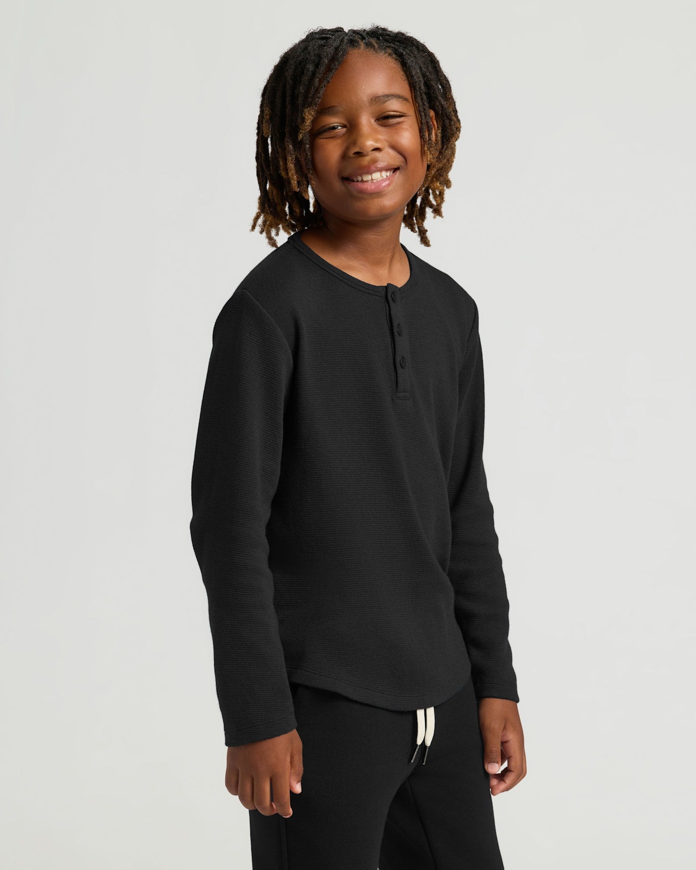 Child in Boys' Waffle Long Sleeve Henley, black top, smiling.