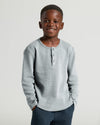 Boy in Boys' Waffle Long Sleeve Henley, smiling, hands in pockets.