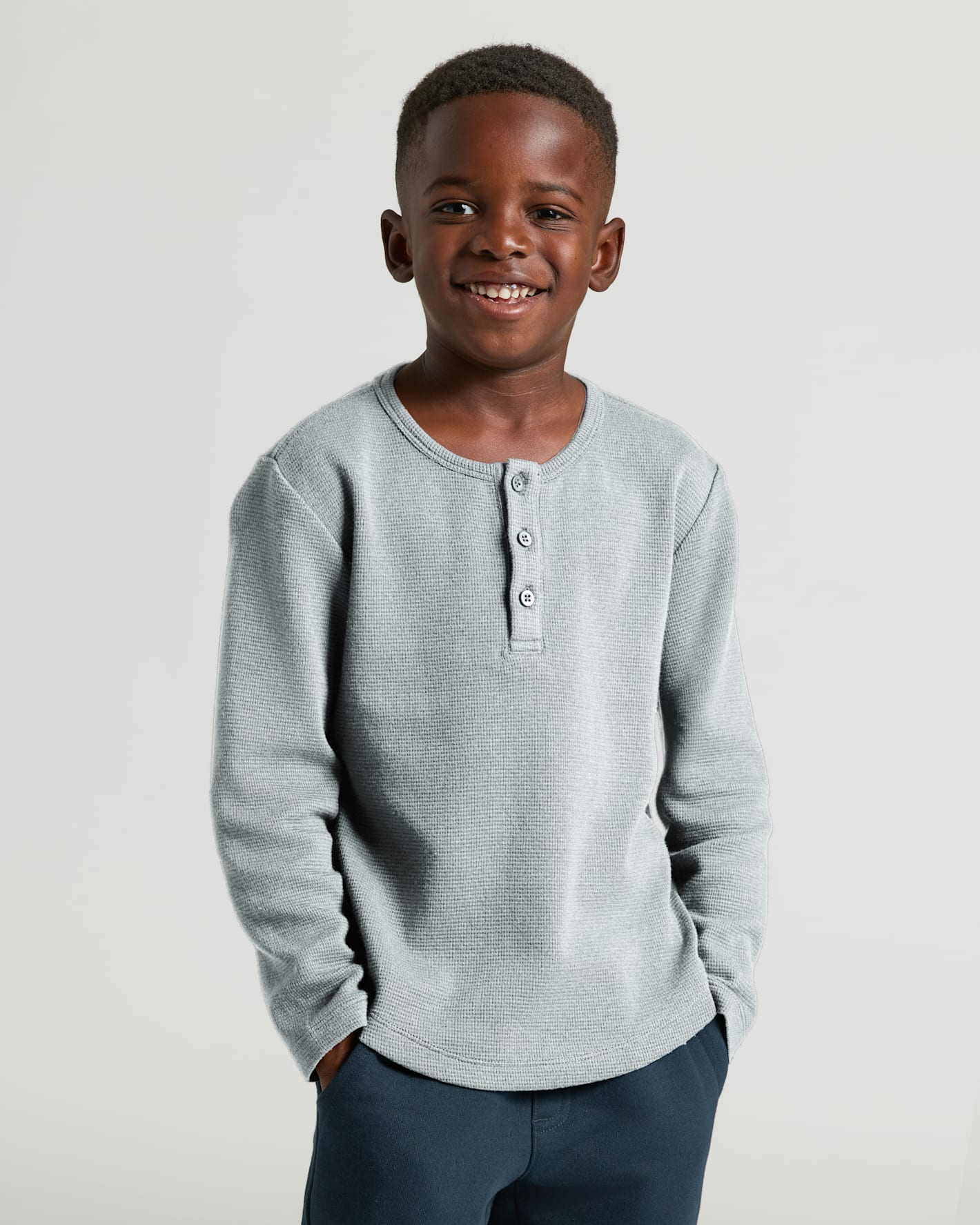 Boy in Boys' Waffle Long Sleeve Henley, smiling, hands in pockets.