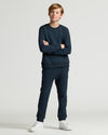 Person wearing a navy blue tracksuit with white sneakers on a light gray background