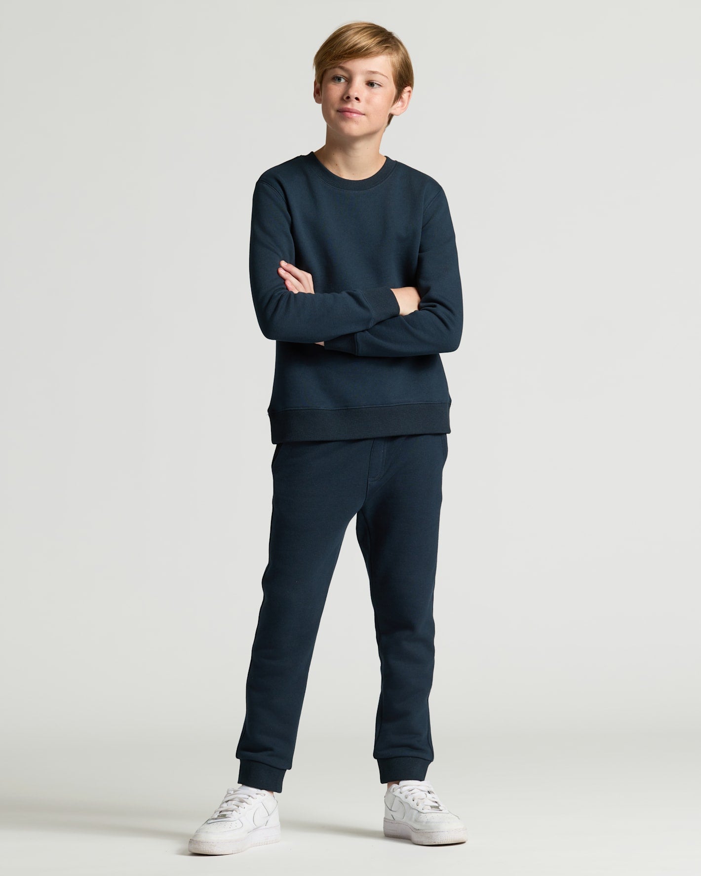 Person wearing a navy blue tracksuit with white sneakers on a light gray background