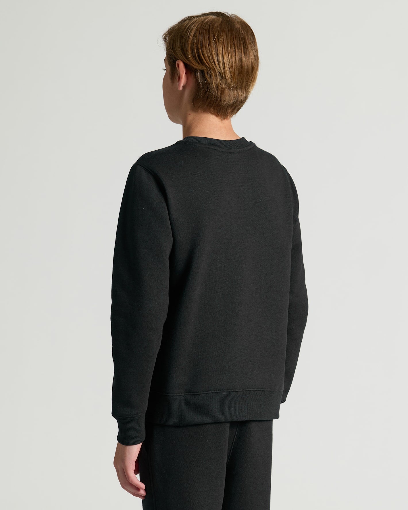 Person wearing a black sweatshirt and pants on a light gray background