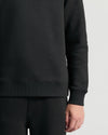 Person wearing a black hoodie and pants on a light gray background