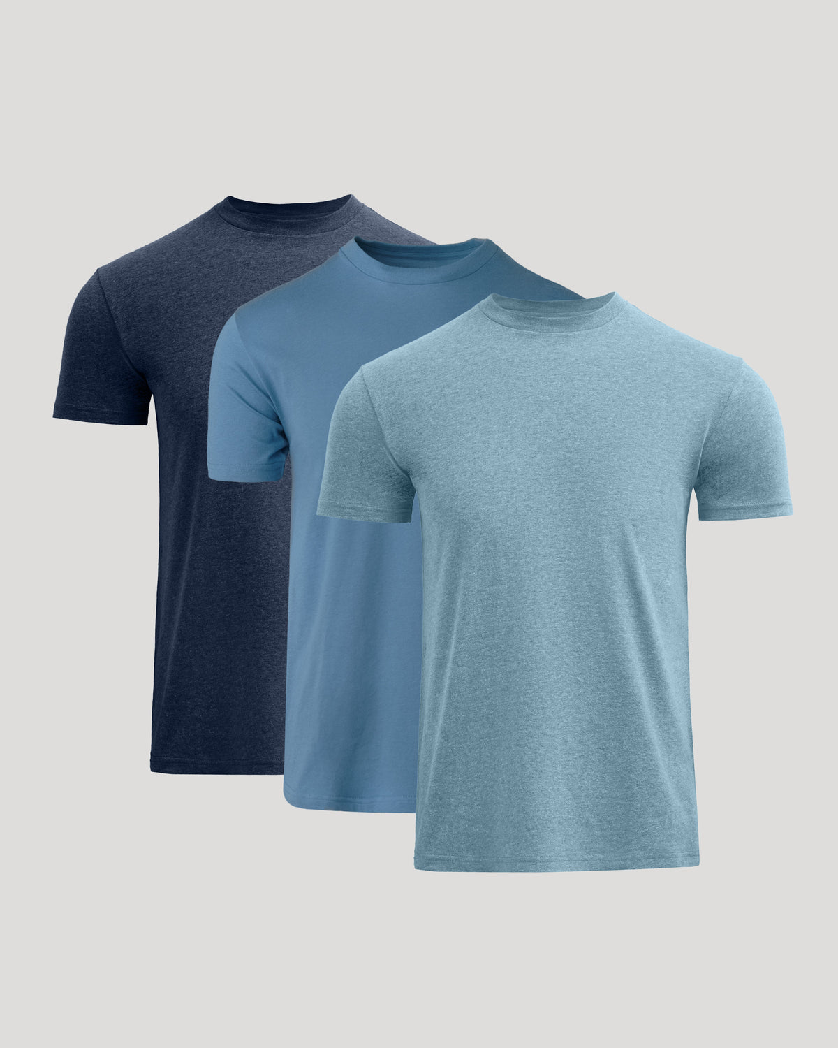 Three short-sleeve crew-neck t-shirts in navy, medium blue, and heather light blue, arranged in a staggered overlapping layout on a light gray background.