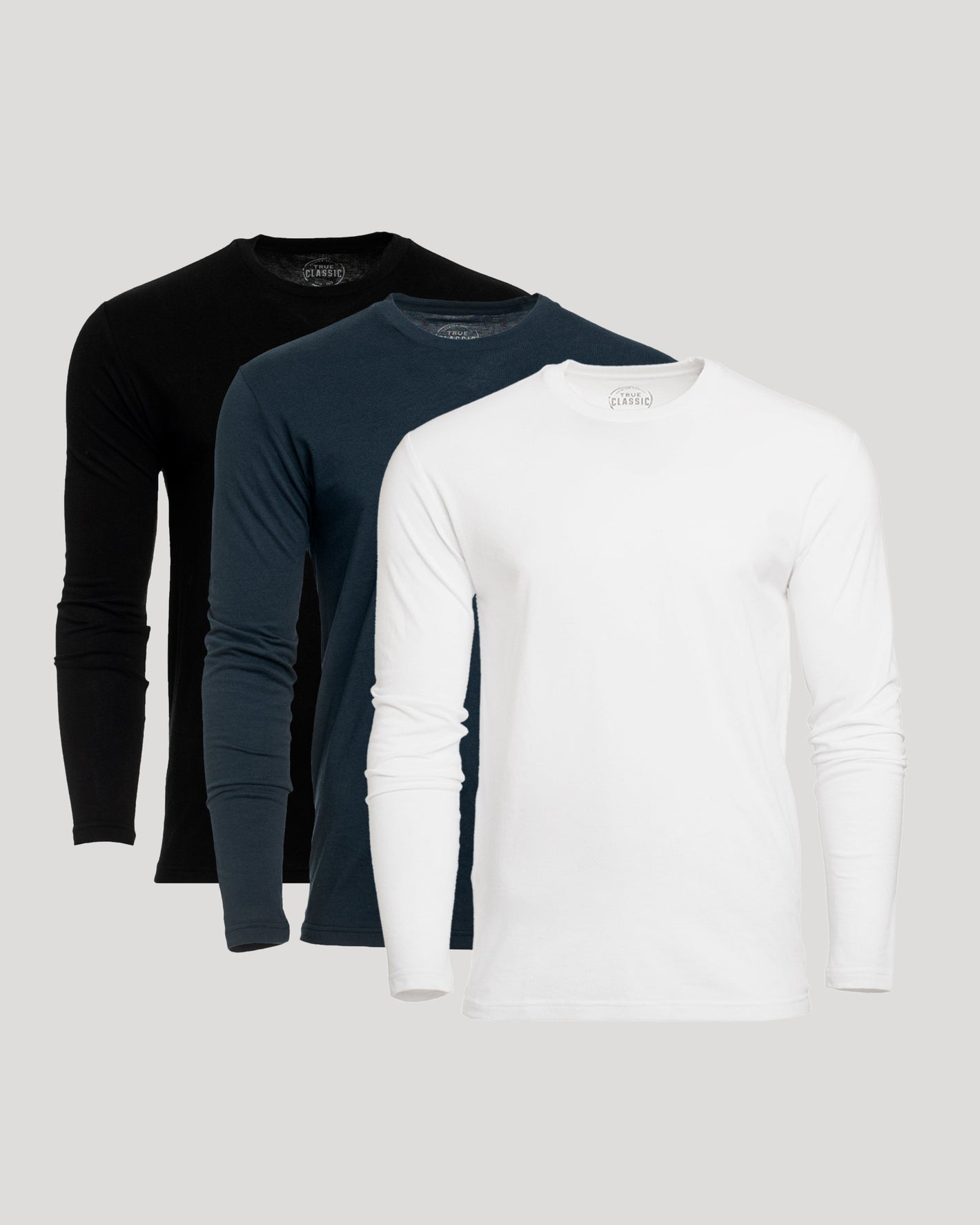 Three long-sleeve shirts in black, navy, and white on a light gray background