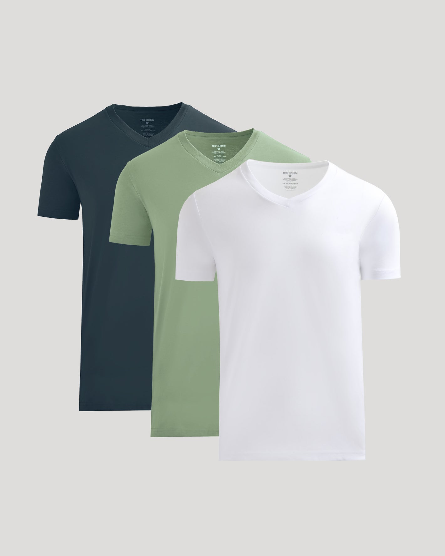 Three plain t-shirts in navy, green, and white on a light gray background