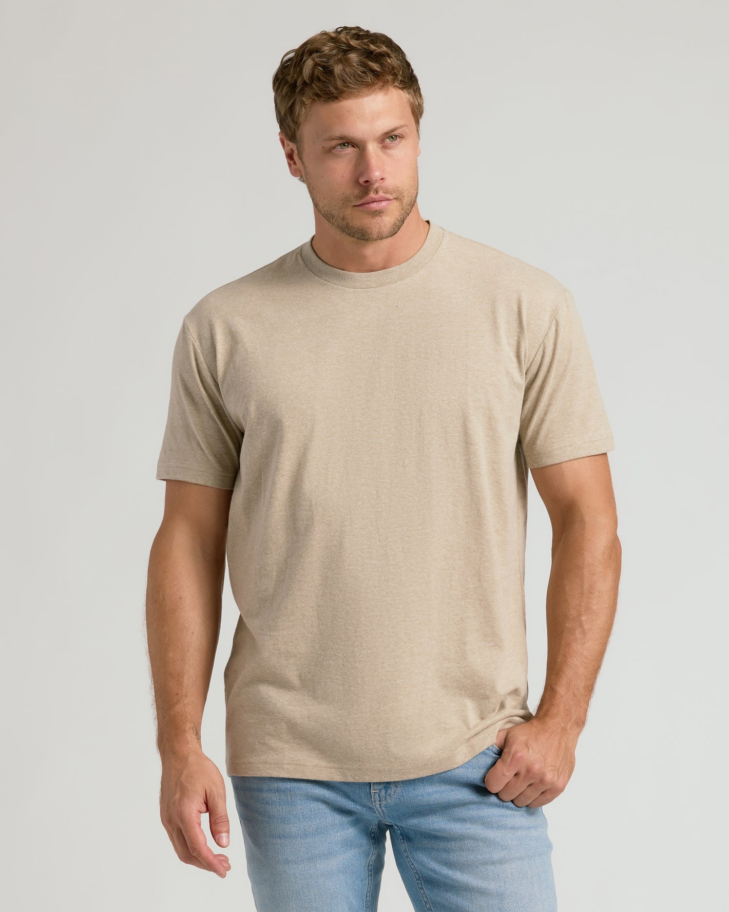 Man wearing a beige t-shirt and light blue jeans against a plain background