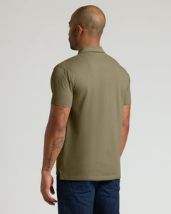 True ClassicA man shown from the back wearing a short-sleeve polo shirt in olive green, paired with dark blue jeans, against a plain light gray studio background.