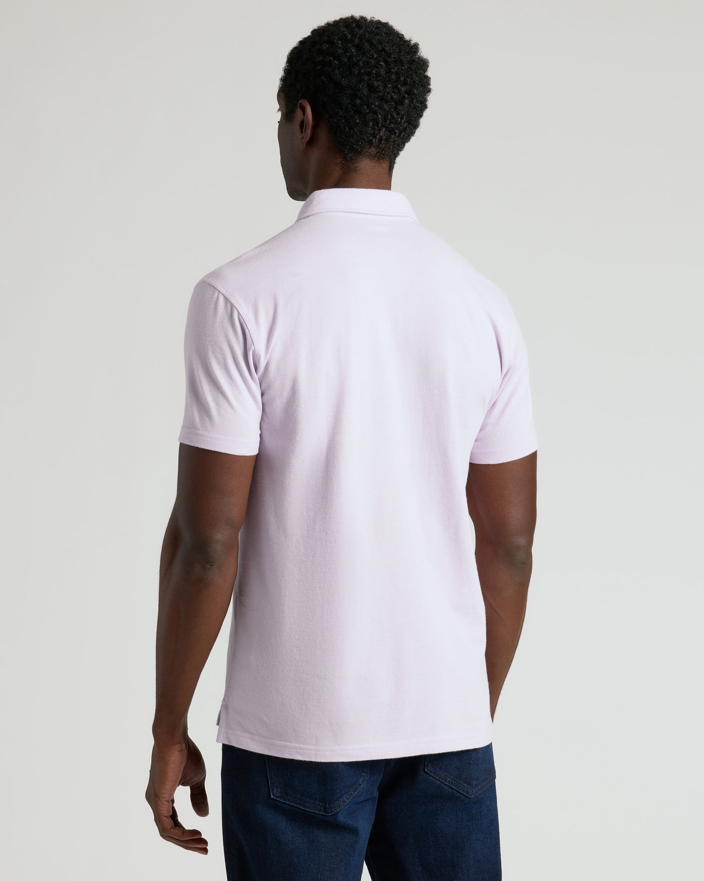 Man wearing Heather Orchid Classic Polo, back view, against light background.