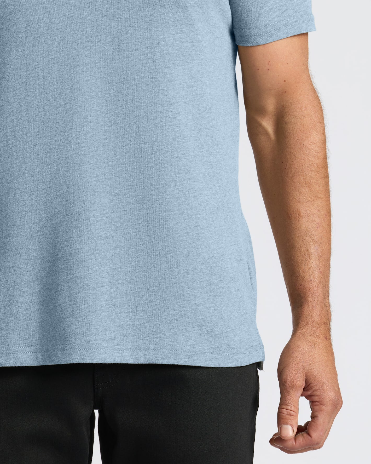 Close-up of a person wearing a light heather blue short-sleeve t-shirt and black pants against a plain light gray background.