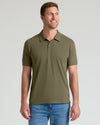 A man wearing an olive green short-sleeve polo shirt and blue jeans, standing against a light gray studio background.