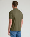 A man viewed from the back wearing an olive green short-sleeve polo shirt and blue jeans, standing against a light gray studio background.