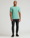 A man modeling a short-sleeve crewneck t-shirt in mint green, paired with black joggers and black sneakers, standing against a light gray studio background.