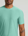 A close-up of a man wearing a short-sleeve crewneck t-shirt in a heathered mint green color, shown from the chin down against a light gray background.