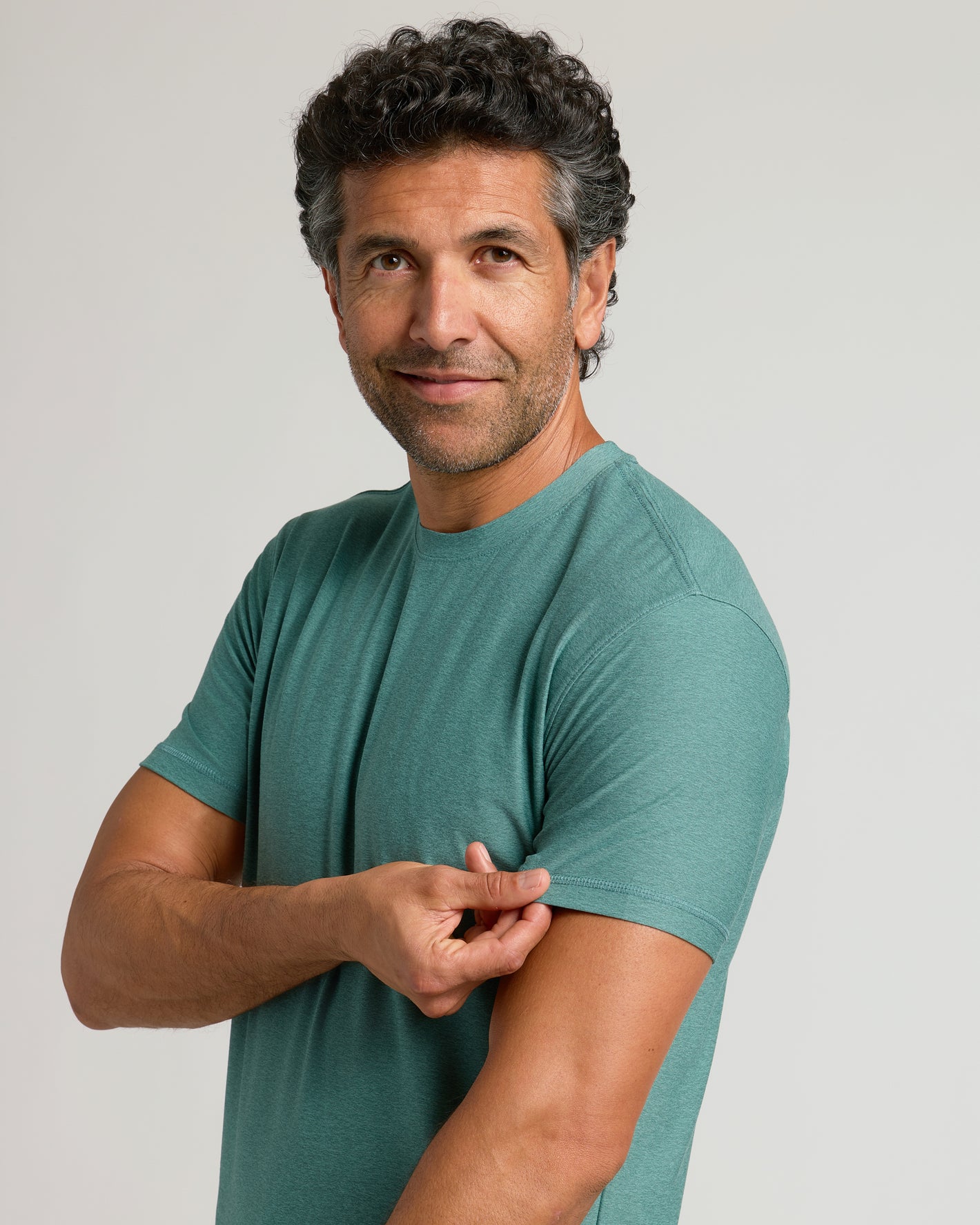 Man wearing Evergreen Active Crew Neck Tee, gently tugging sleeve, smiling.