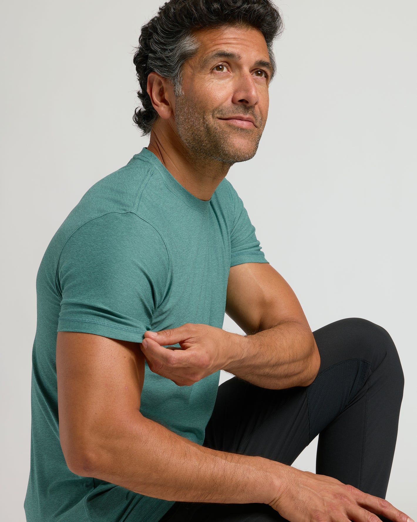 Man wearing Evergreen Active Crew Neck Tee, seated thoughtfully.