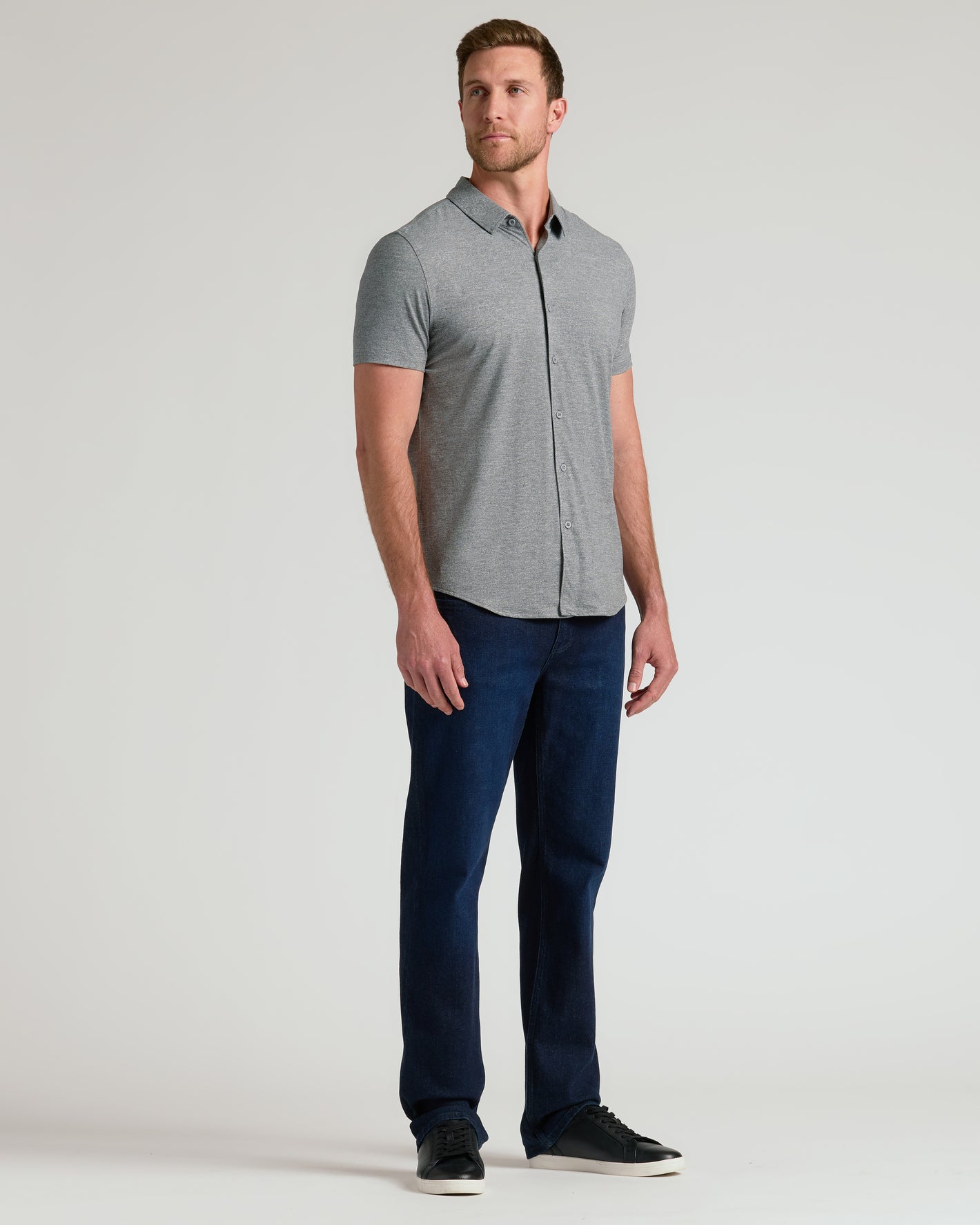 Man wearing Heather Gray Short Sleeve Comfort Knit Shirt, dark jeans, black sneakers.