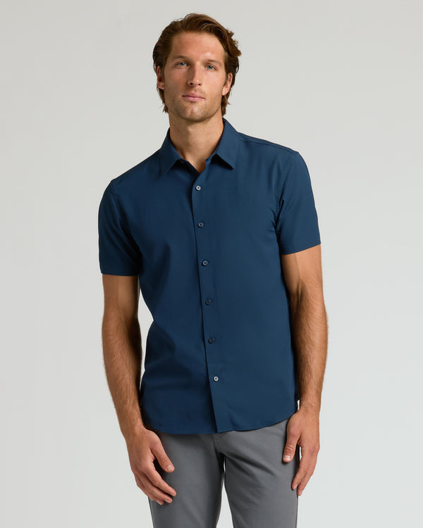 Man wearing Navy Performance Dress Shirt and gray trousers, posed casually.