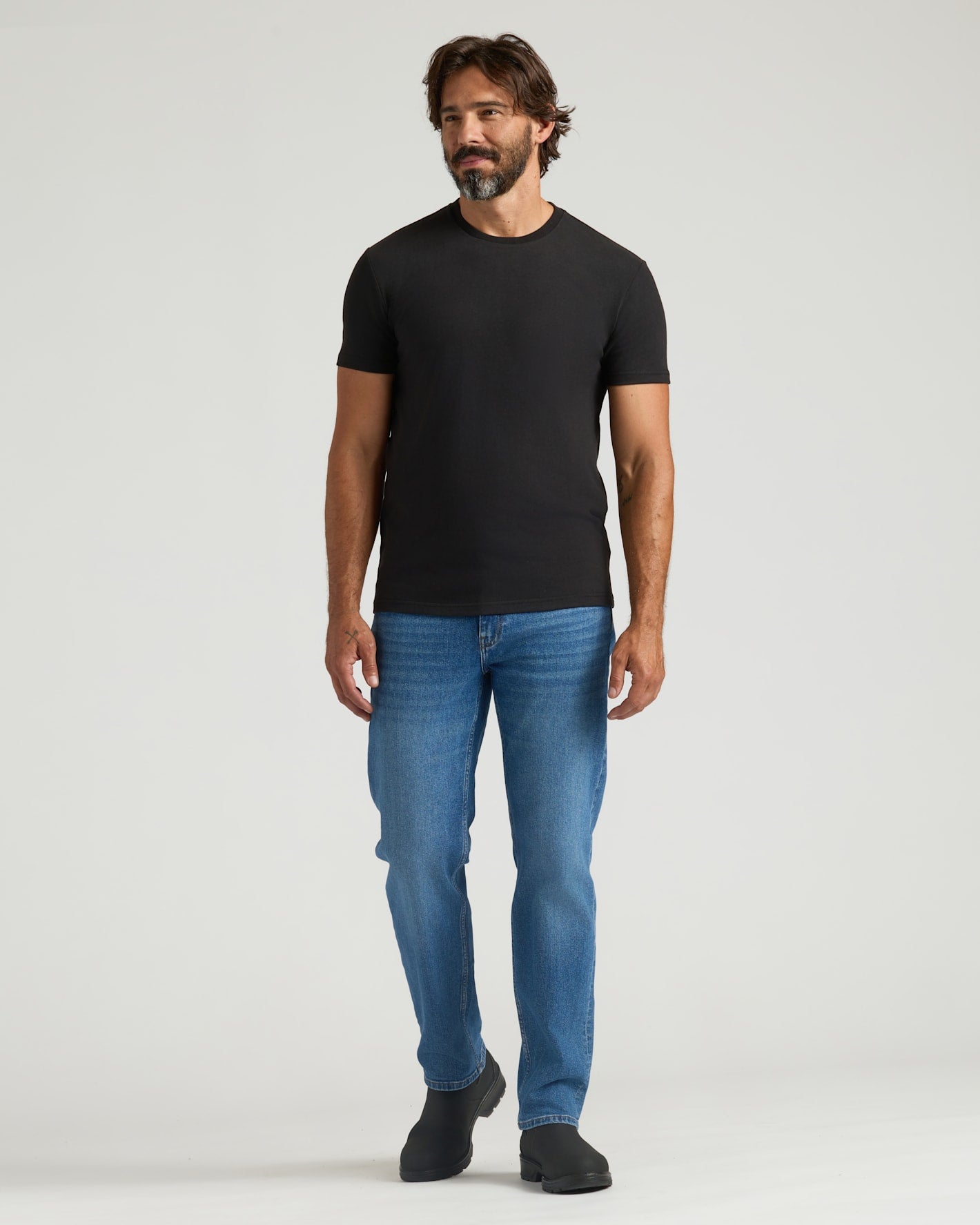 Man wearing a black t-shirt and blue jeans on a white background