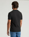 Man wearing a black t-shirt and blue jeans on a light gray background