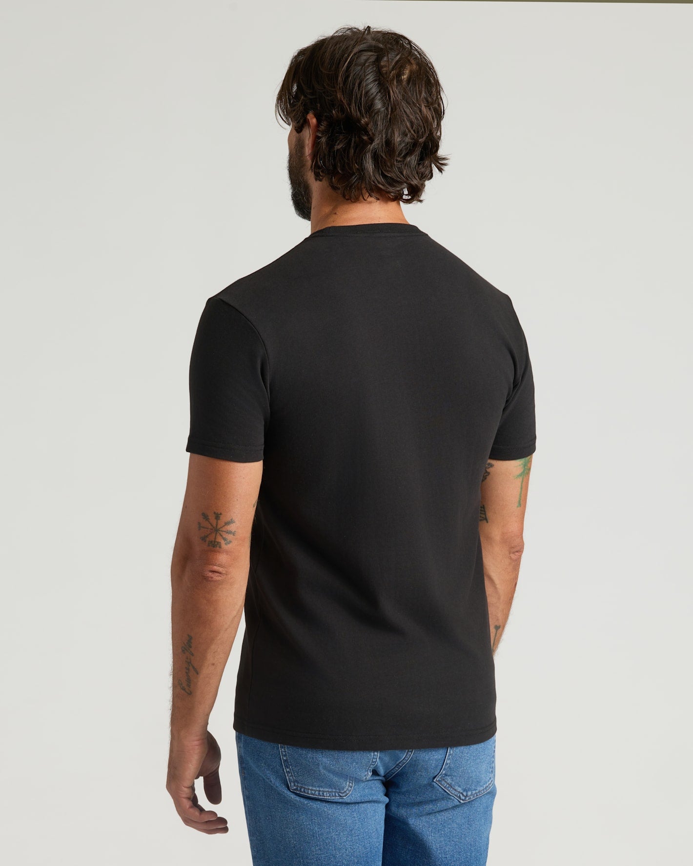 Man wearing a black t-shirt and blue jeans on a light gray background