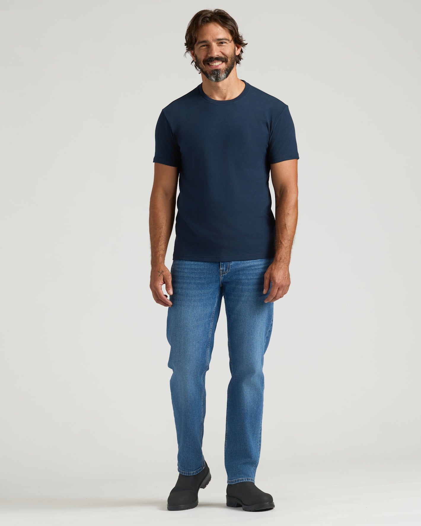 Man wearing a navy blue t-shirt and blue jeans on a white background
