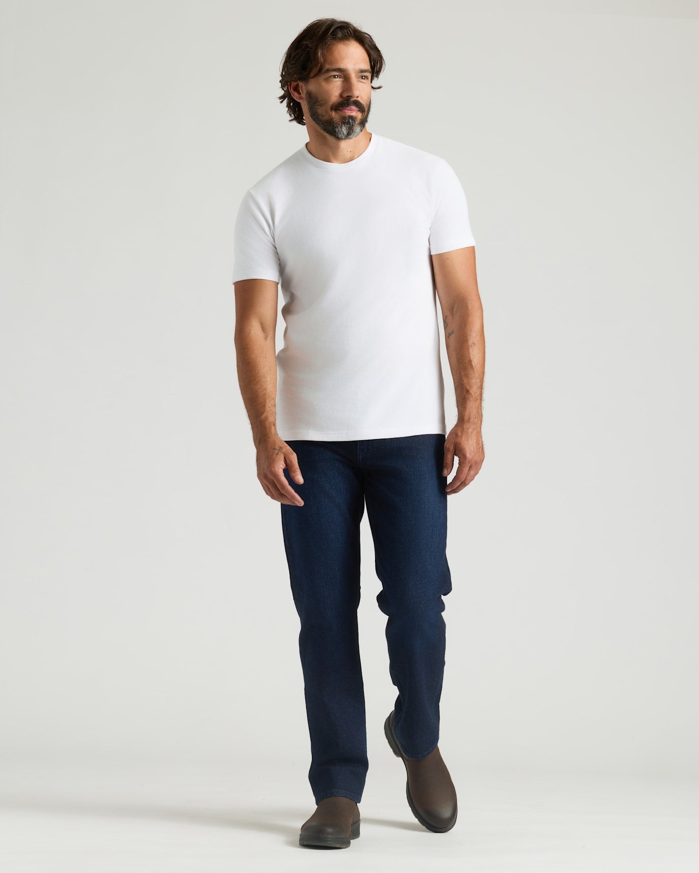 Man wearing a white t-shirt and blue jeans on a light gray background