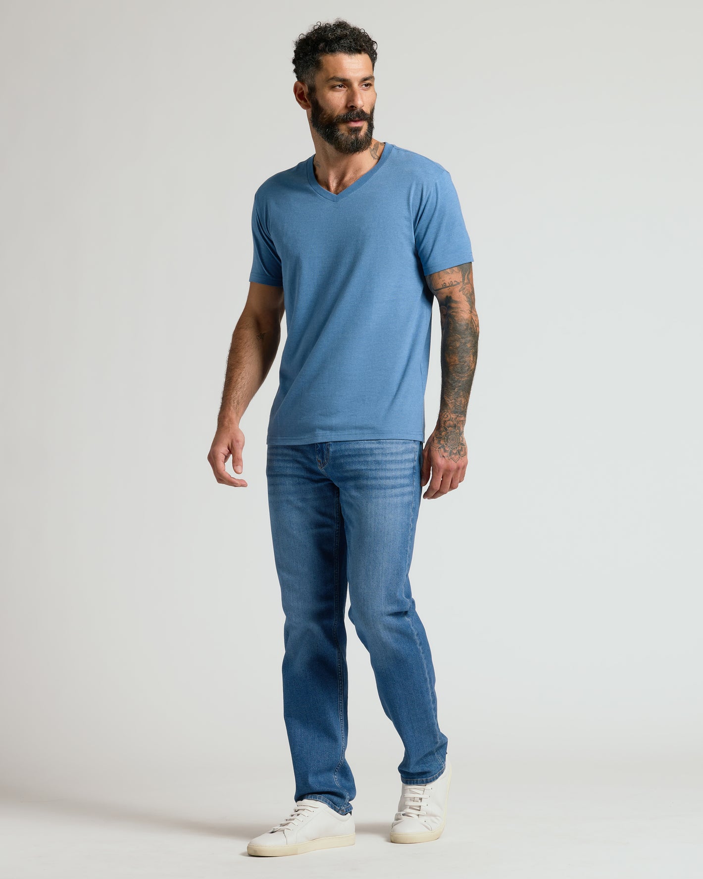 Man wearing Dark Heather Blue Lake V Neck Tee, jeans, and sneakers.