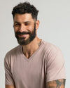 Man in Light Heather Slate Mauve Classic V-Neck, smiling with tattoos visible.