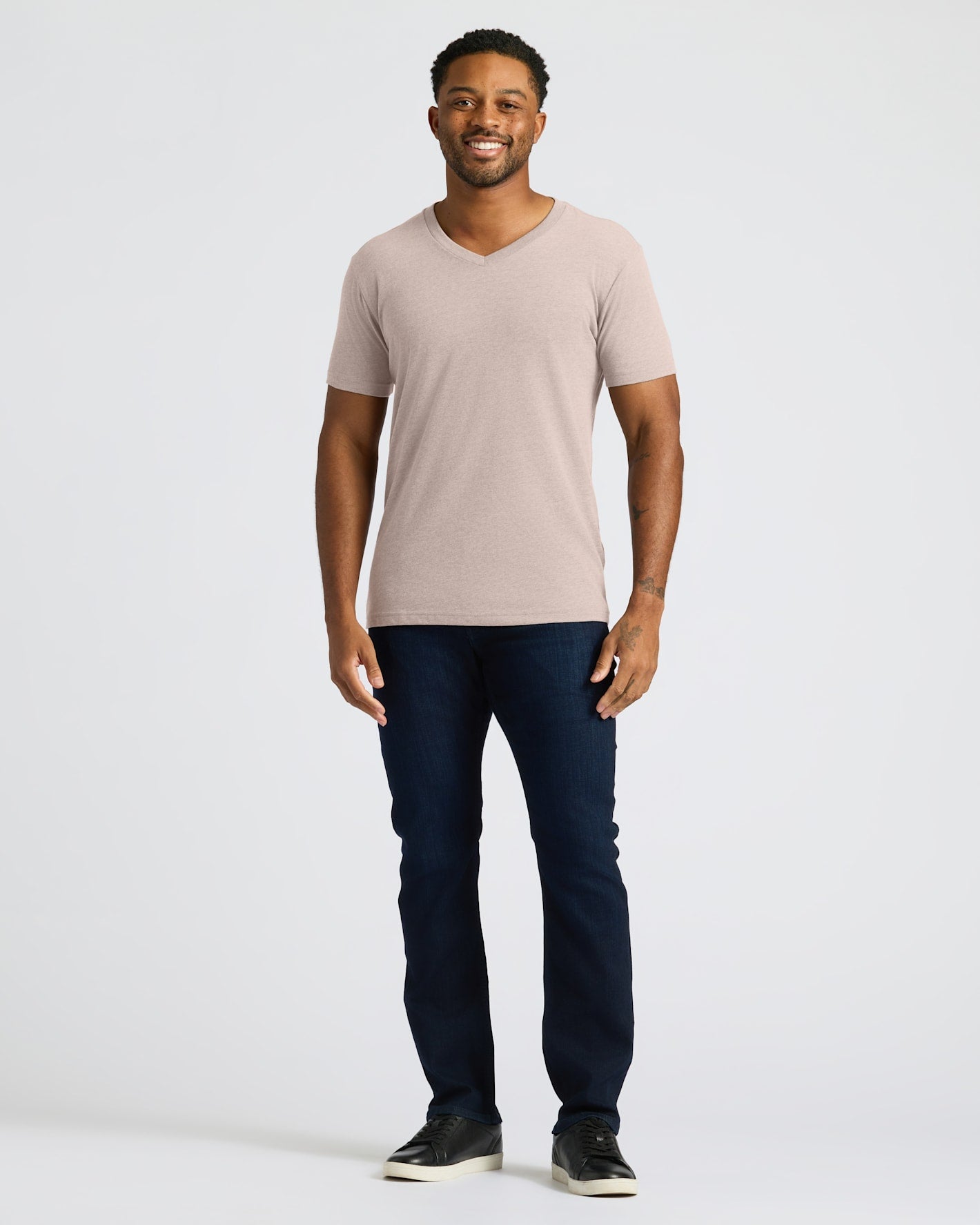 Man wearing a beige t-shirt and dark jeans on a white background