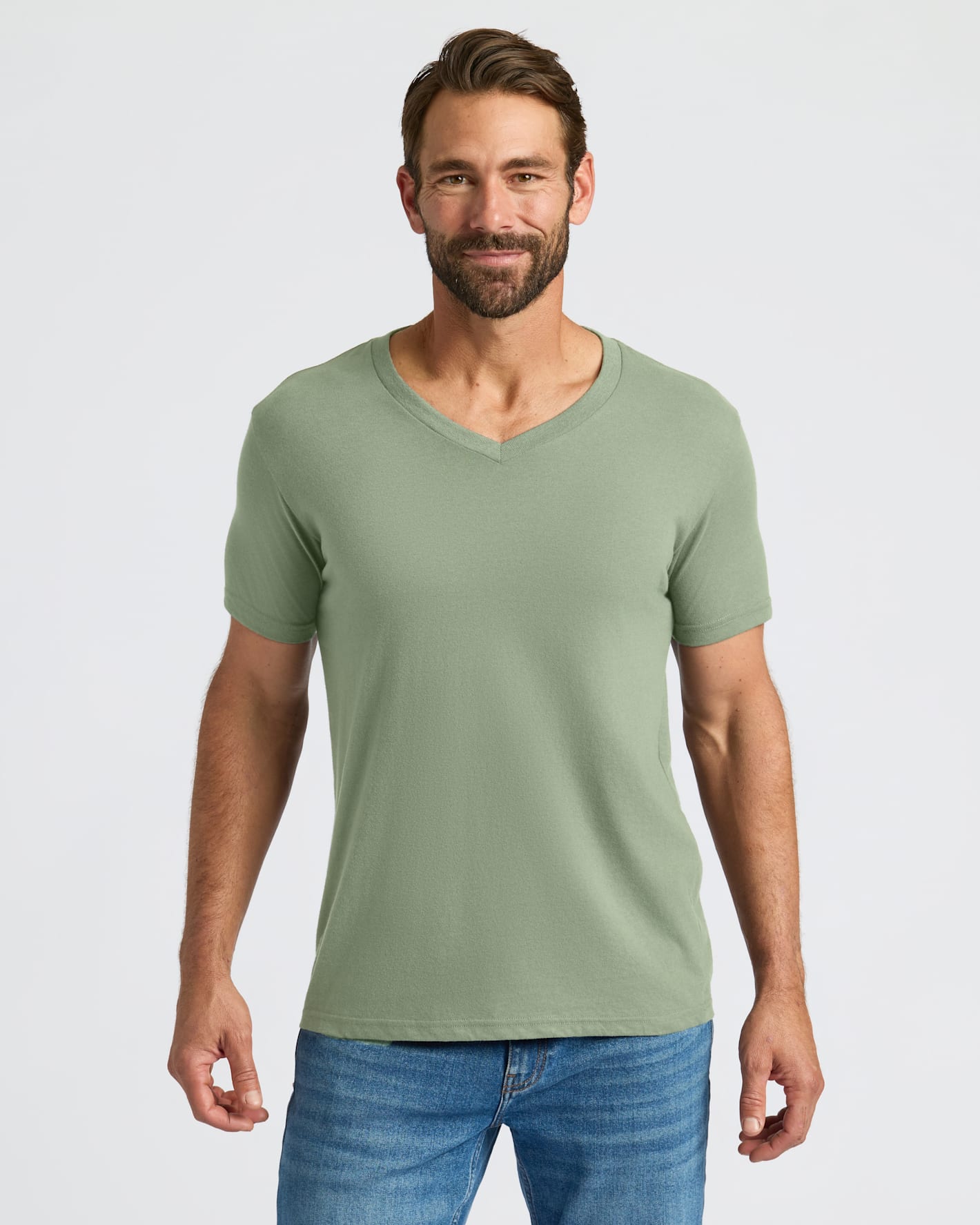 Man wearing a green t-shirt and blue jeans on a light gray background