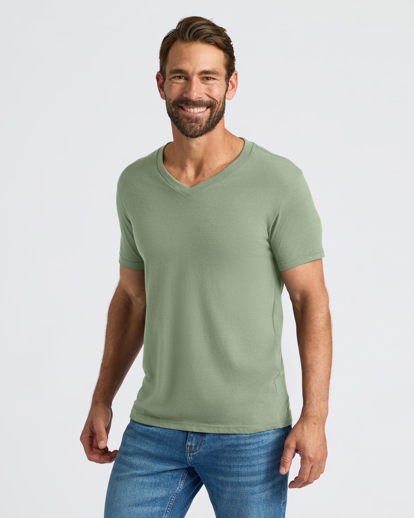 Man wearing a green t-shirt and blue jeans on a light gray background