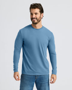 True ClassicA smiling man wearing a light blue long-sleeve crewneck shirt and blue jeans, standing against a light gray studio background.