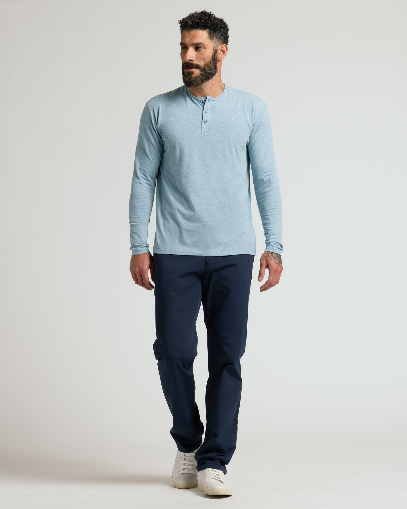 Man in Heather Sapphire Classic Long Sleeve Henley, navy pants, sneakers.