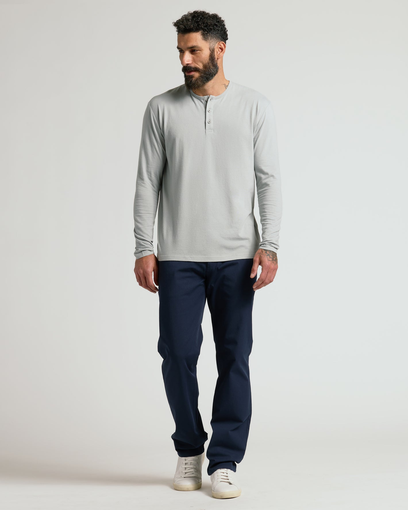 Male model wearing Steel Classic Long Sleeve Henley, navy trousers, white sneakers.