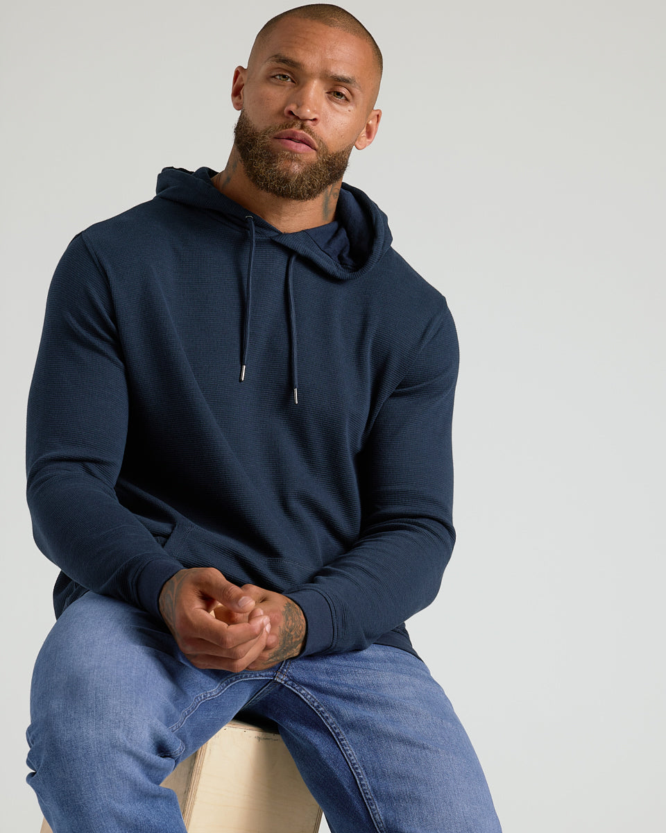 Man wearing Heather Gray & Navy Waffle Hoodie, seated, showing hoodie features.