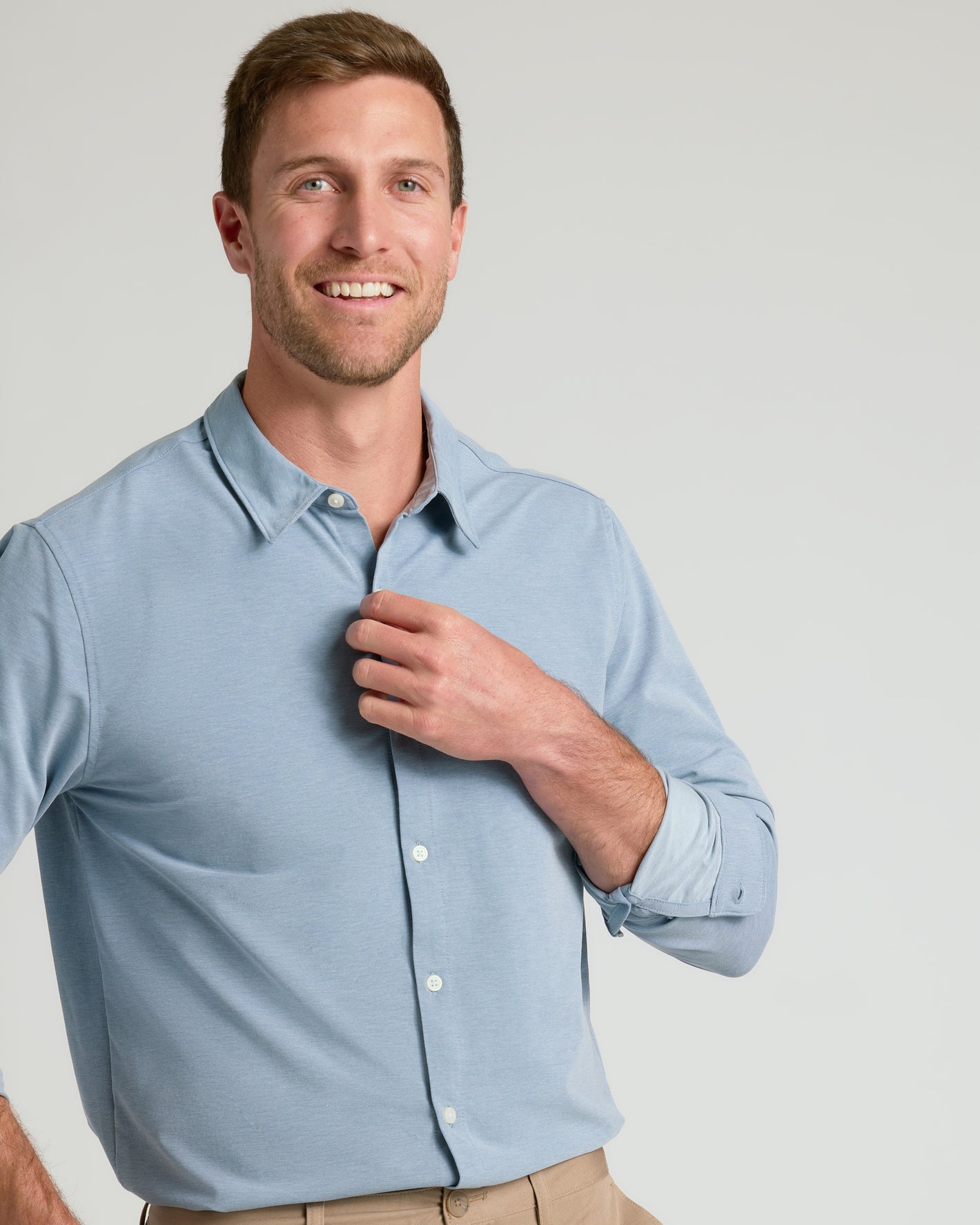 Man wearing Blue Stretch Oxford 2.0, adjusting collar, beige pants visible.